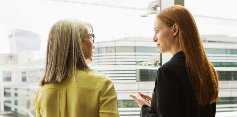 Two women have a discussion while looking out a window