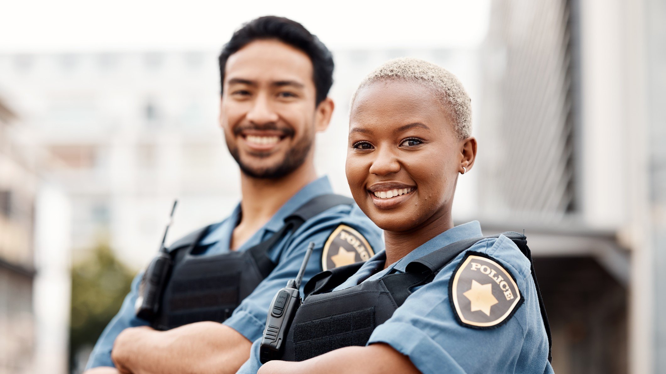 Two police smile as they stand in front of their car.