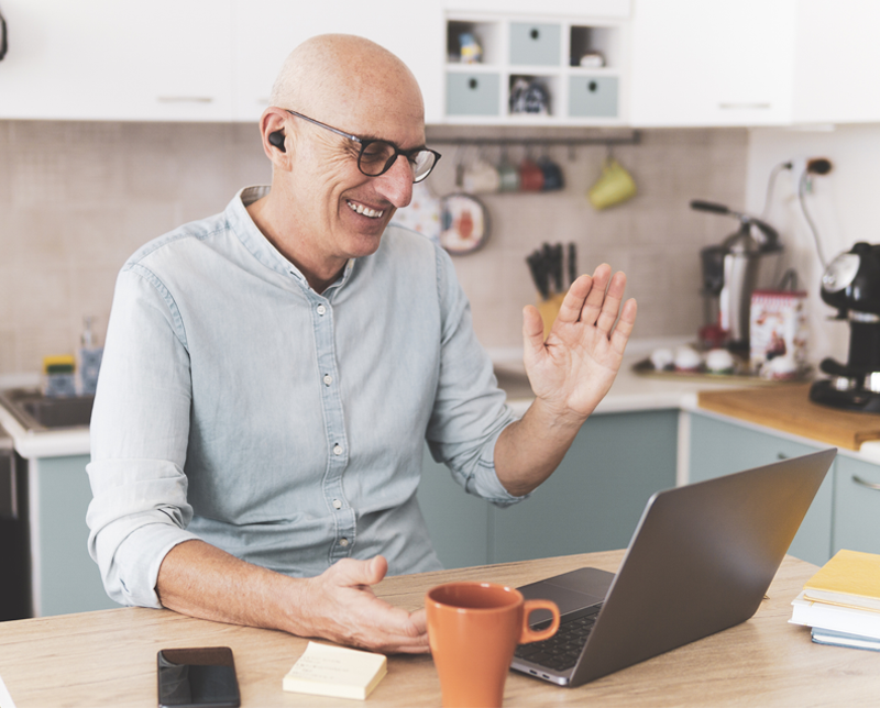 A man waves to the camera while he's in a video meeting