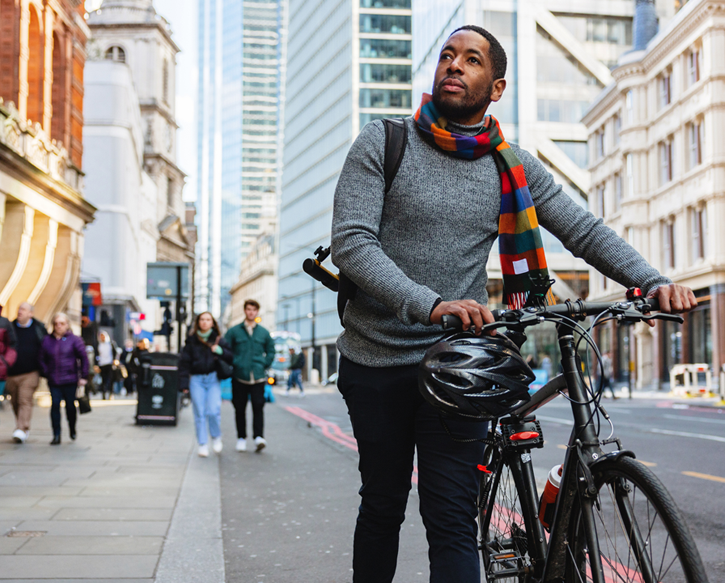 A man walks his bike down the street in the city.