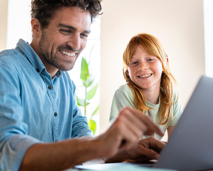 A smiling man works at home with his daughter watching.